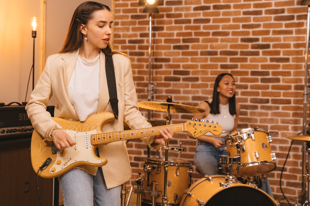 Two women enjoying a jam session with guitar and drums in a cozy music studio.
